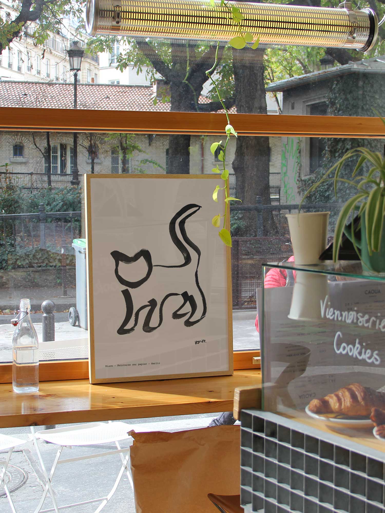 Affiche Miaou de Haritz dans un coffee shop parisien lumineux et branché avec vue sur rue.