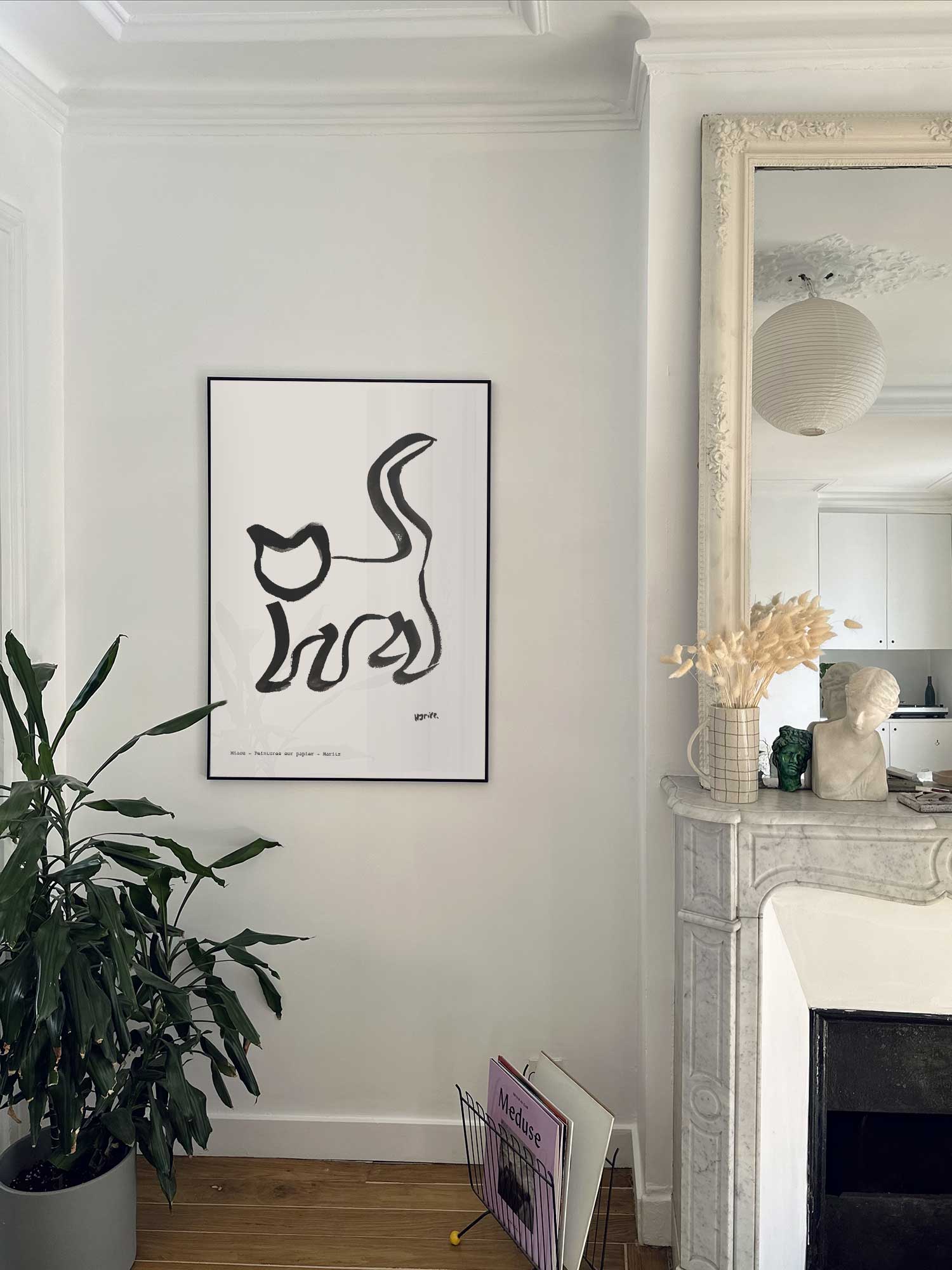 Affiche Miaou de Haritz accrochée au mur près d'une cheminée en marbre dans un appartement parisien.