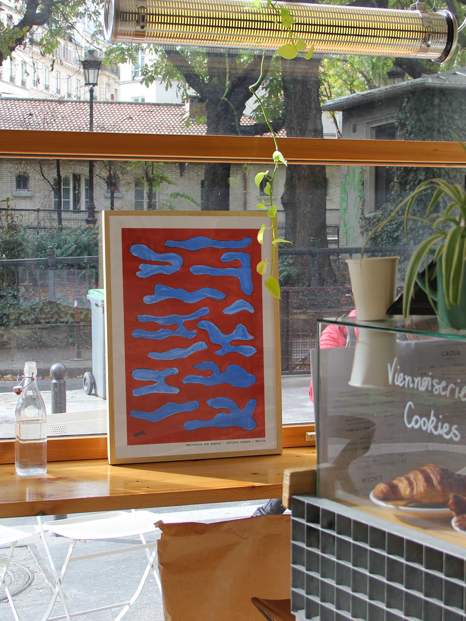 Affiche Reflets rouges de Haritz dans un coffee shop parisien lumineux et branché avec vue sur rue.