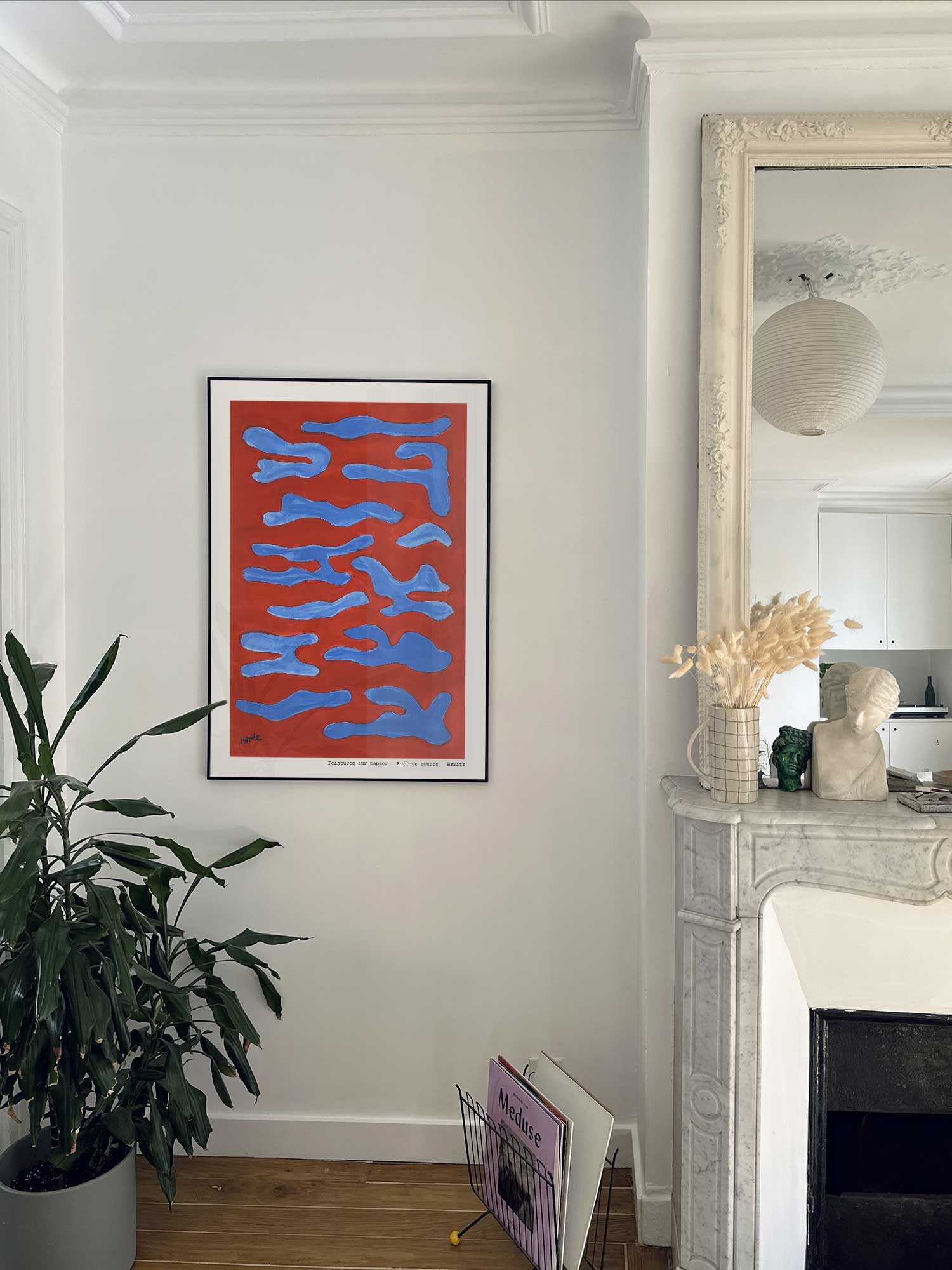Affiche Reflets rouges de Haritz accrochée au mur près d'une cheminée en marbre dans un appartement parisien.