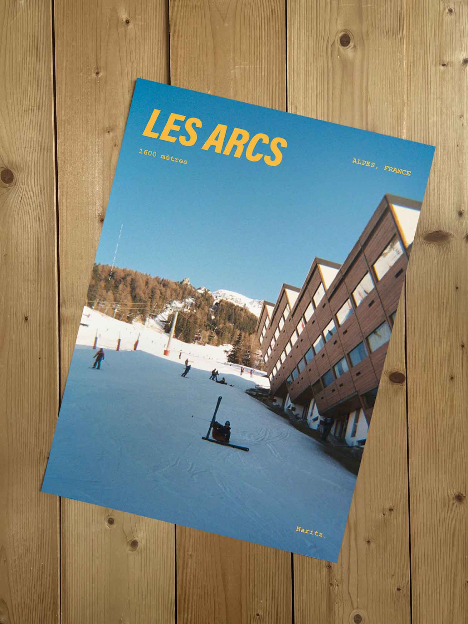 Affiche Les Arcs vintage sans cadre posée sur parquet bois — pistes et architecture d'Arc 1600, photographie argentique Haritz