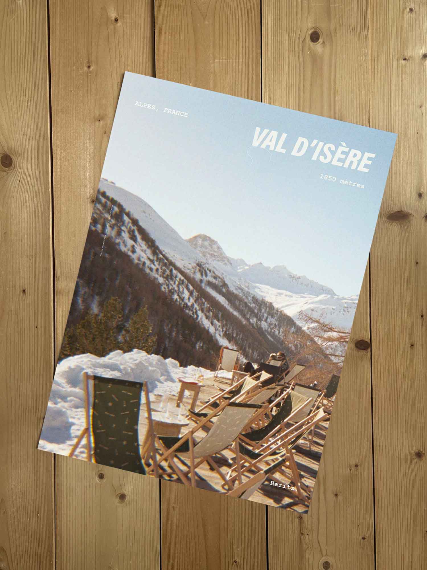 Affiche Val d'Isère vintage sans cadre posée sur parquet bois — rangée de transats en bois sur terrasse enneigée, photographie argentique Haritz