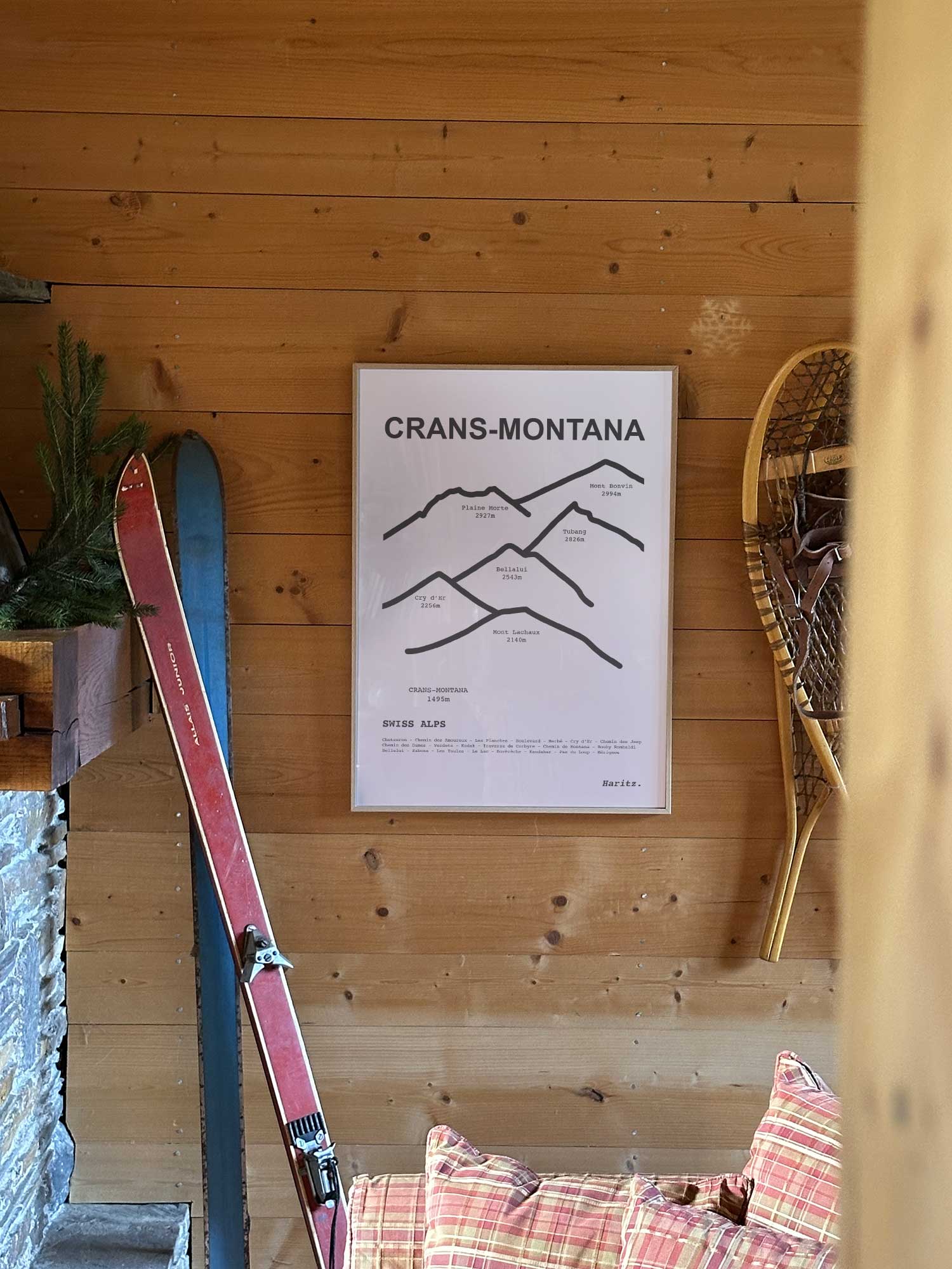 Affiche Crans-Montana représentant les sommets de la station, accrochée au mur d’un salon de chalet avec skis vintage et raquettes à neige, décoration montagne Haritz.