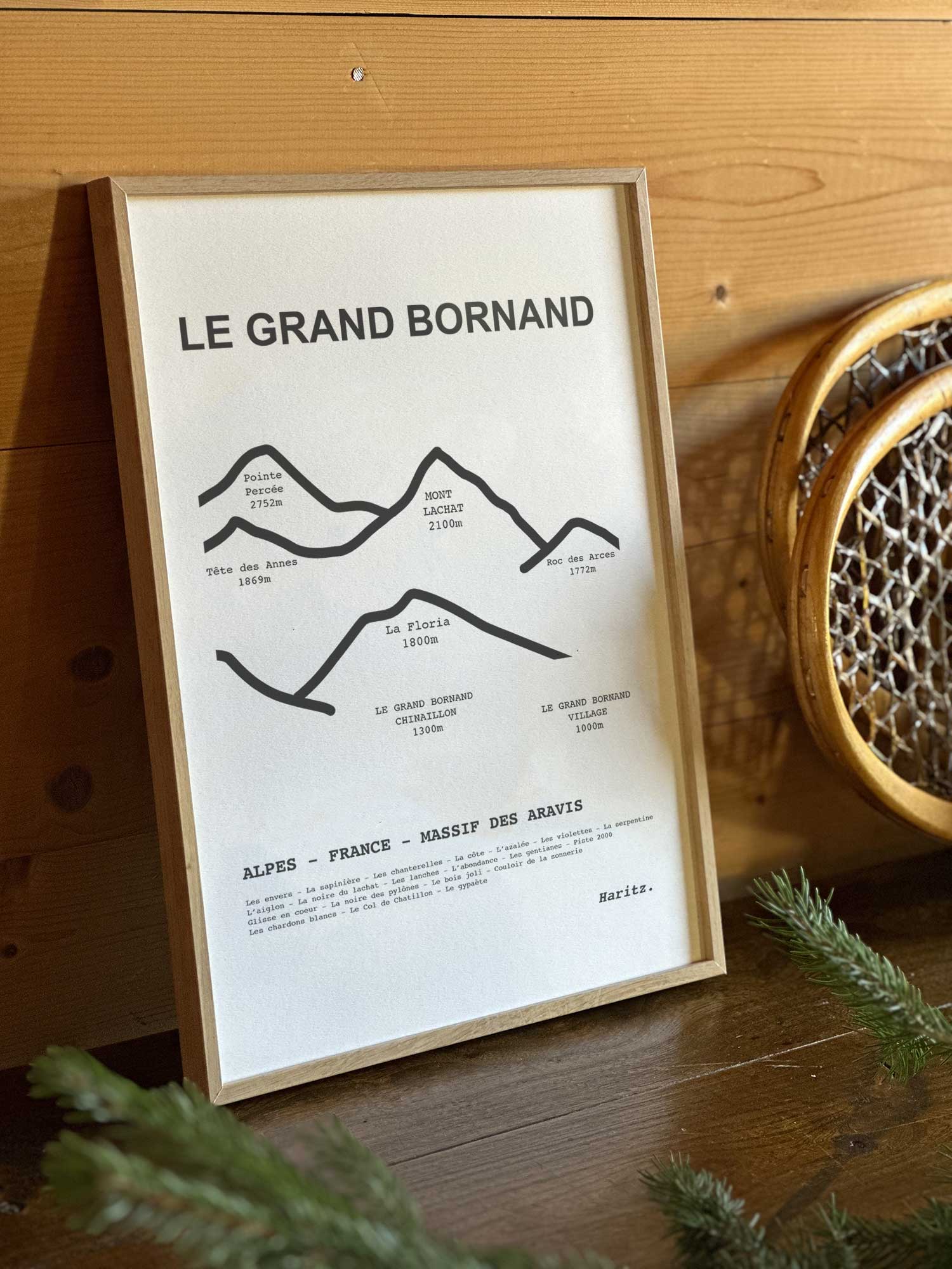 Affiche Le Grand Bornand du tracé topographique des sommets dans un cadre en bois naturel, mise en scène dans une décoration chalet avec objets vintage et raquettes à neige, par Haritz.