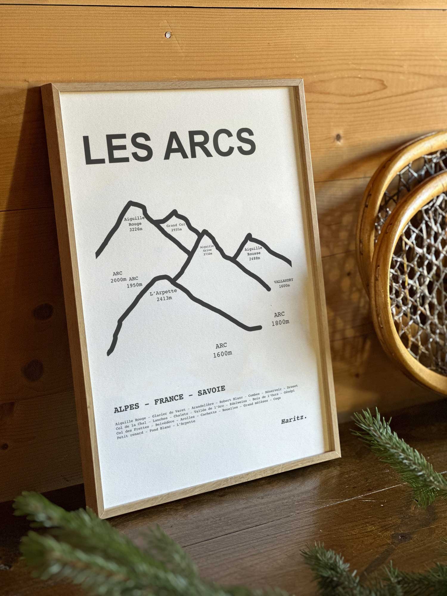 Affiche Les Arcs du tracé topographique des sommets dans un cadre en bois naturel, mise en scène dans une décoration chalet avec objets vintage et raquettes à neige, par Haritz.