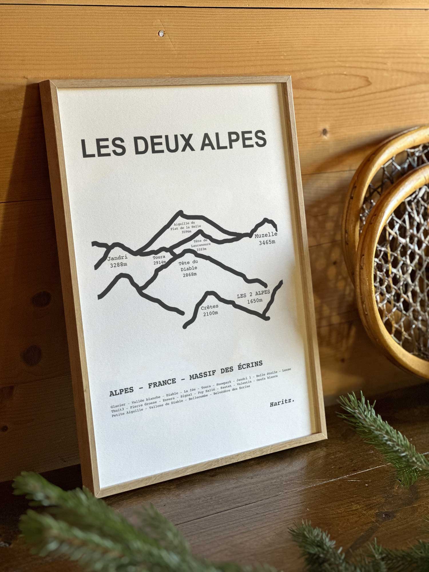 Affiche Les Deux Alpes du tracé topographique des sommets dans un cadre en bois naturel, mise en scène dans une décoration chalet avec objets vintage et raquettes à neige, par Haritz.
