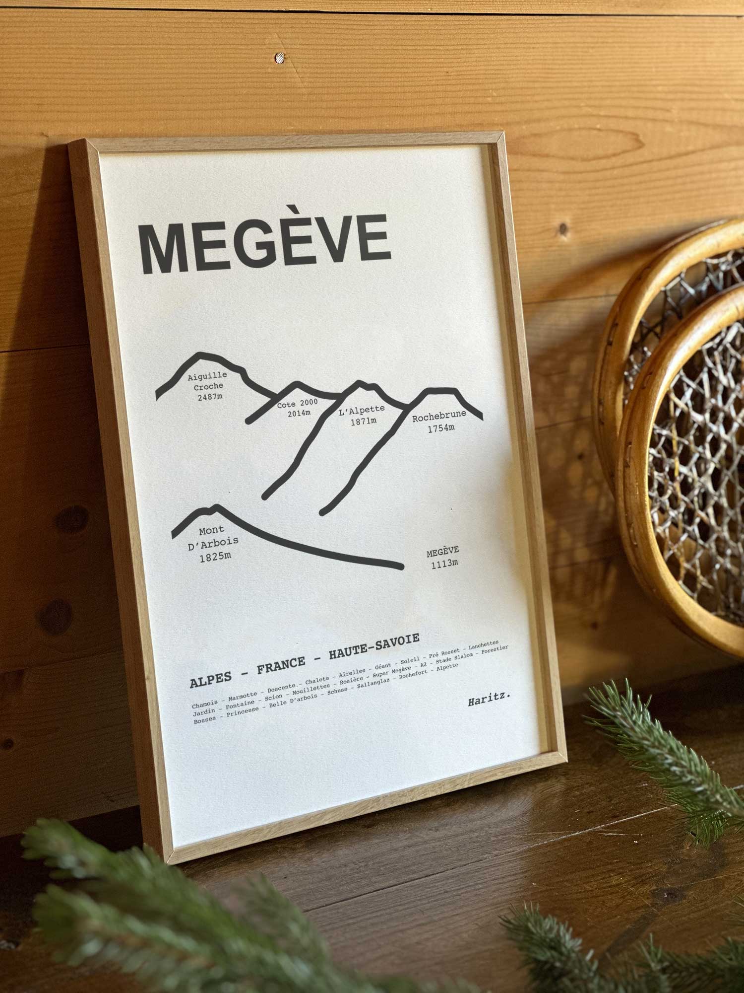 Affiche Megève du tracé topographique des sommets dans un cadre en bois naturel, mise en scène dans une décoration chalet avec objets vintage et raquettes à neige, par Haritz.