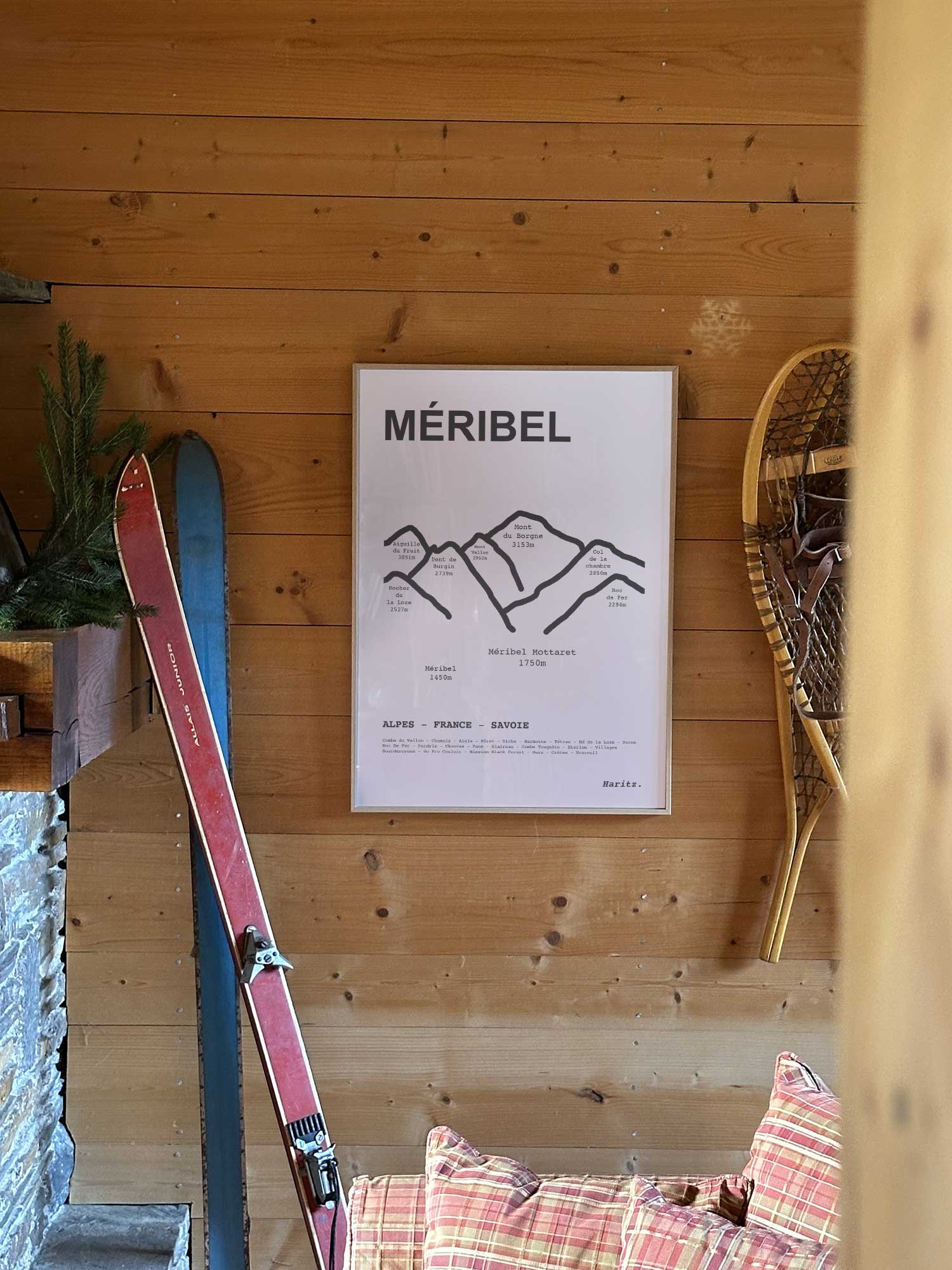 Affiche Méribel représentant les sommets de la station, accrochée au mur d’un salon de chalet avec skis vintage et raquettes à neige, décoration montagne Haritz.