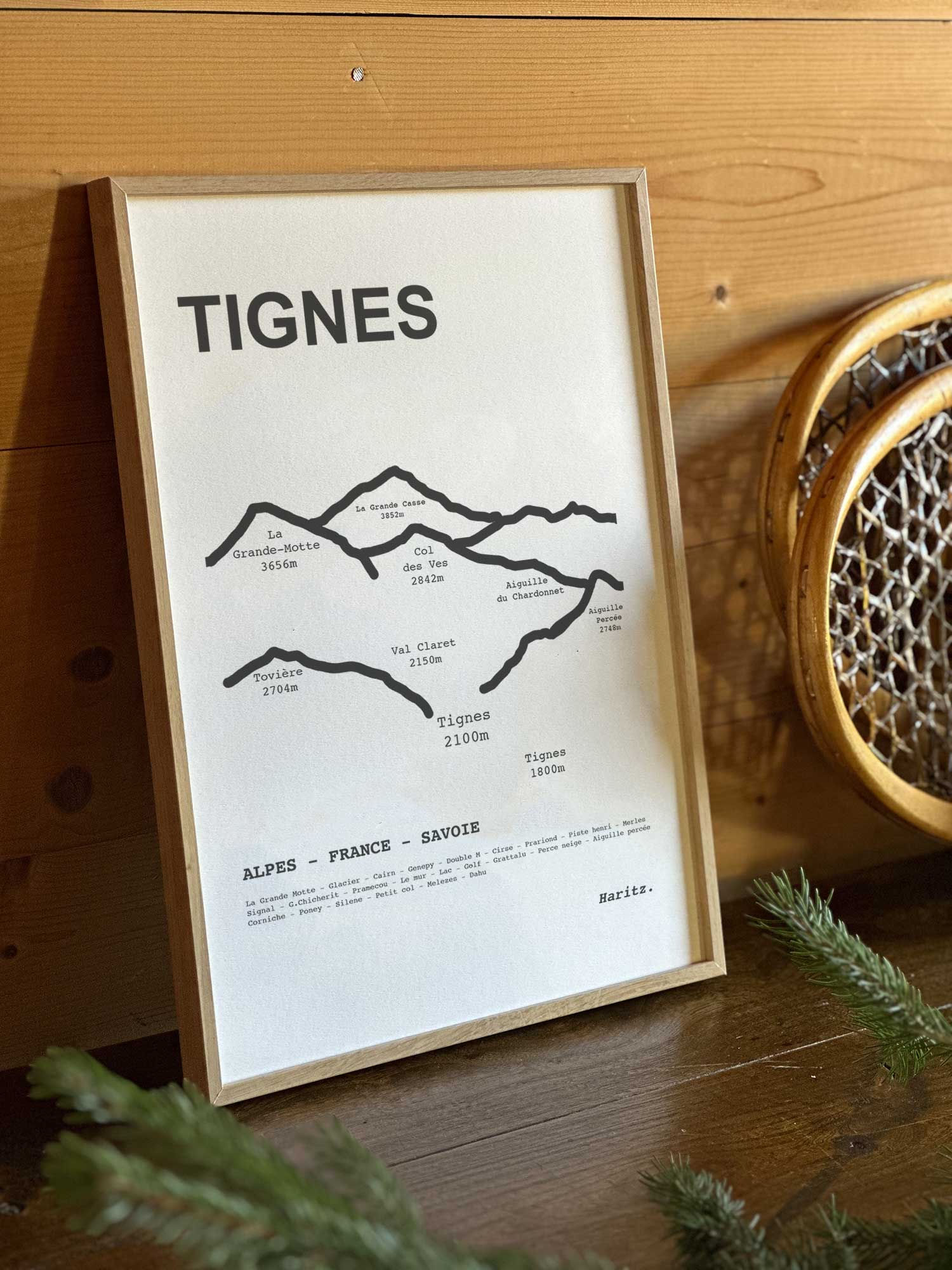 Affiche Tignes du tracé topographique des sommets dans un cadre en bois naturel, mise en scène dans une décoration chalet avec objets vintage et raquettes à neige, par Haritz.