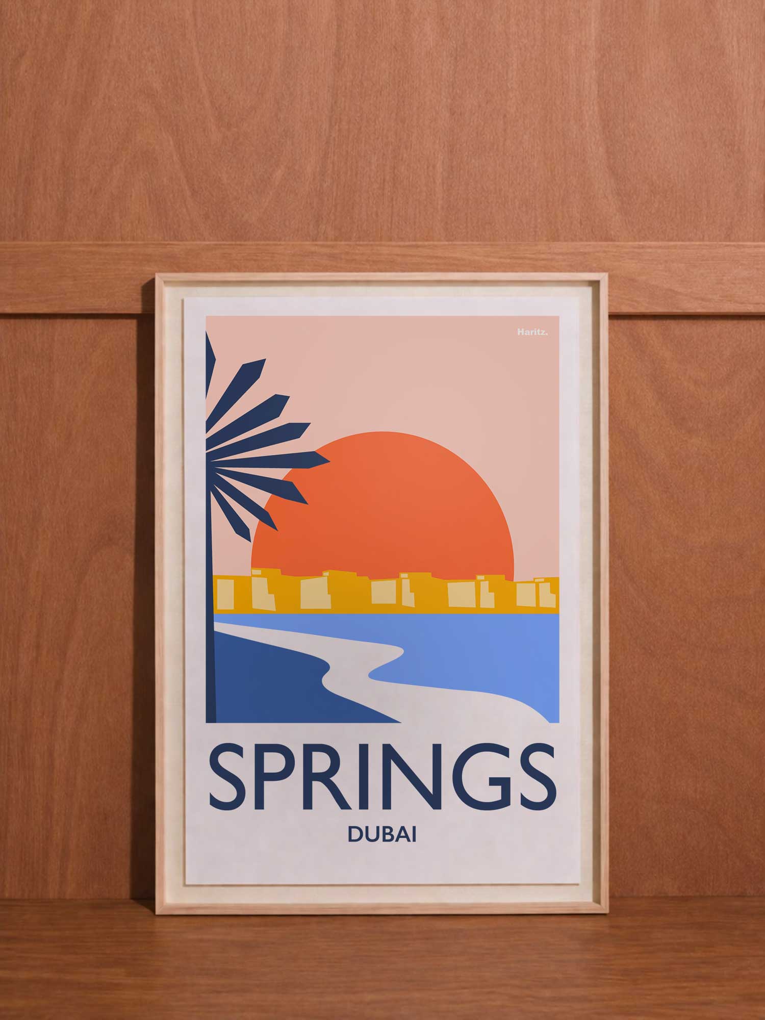 Affiche contemporaine Haritz "Springs Dubai" - design graphique minimaliste rose et bleu marine représentant paysage urbain avec lac, palmier et soleil couchant, cadre bois naturel