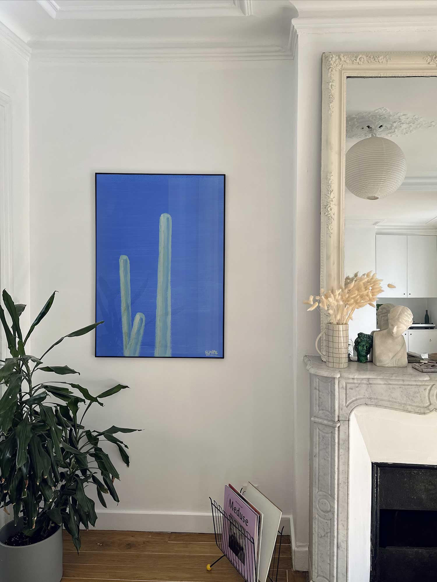 Affiche cactus vert de Haritz accrochée au mur près d'une cheminée en marbre dans un appartement parisien.