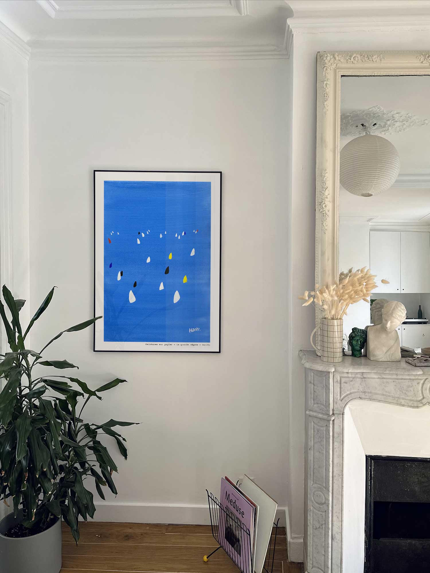 Affiche La grande régate de Haritz accrochée au mur près d'une cheminée en marbre dans un appartement parisien.