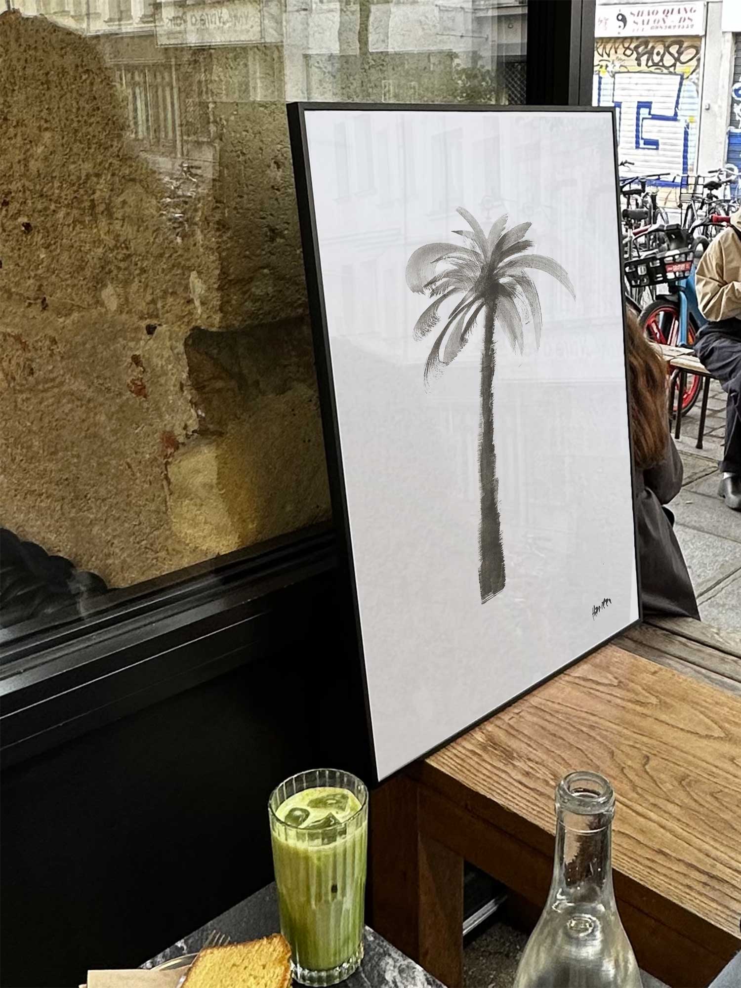 Affiche Palmier2 de Haritz exposée près d'une fenêtre dans un café parisien tendance à côté d'un verre de matcha latte.