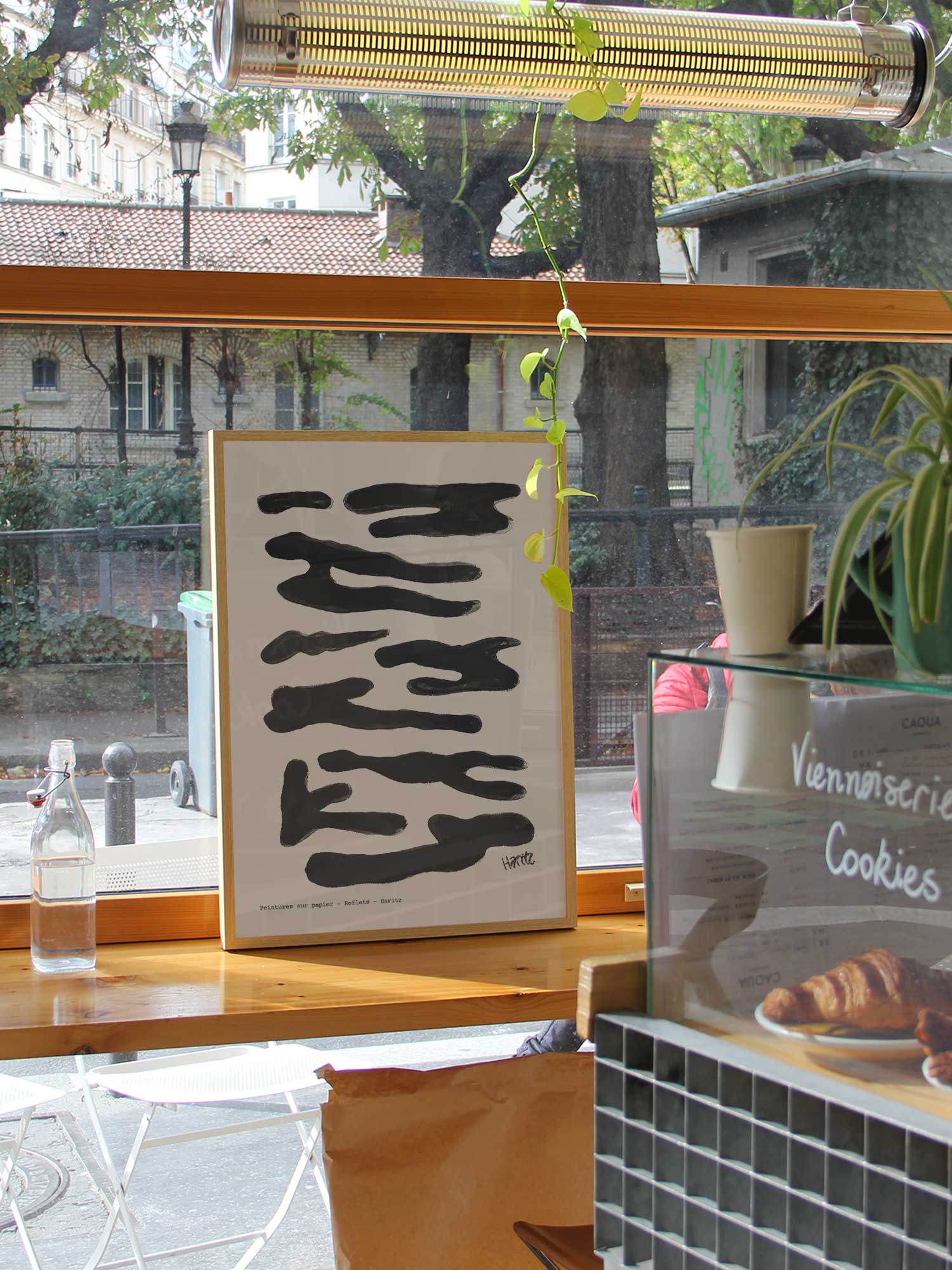Affiche Reflets noirs de Haritz dans un coffee shop parisien lumineux et branché avec vue sur rue.