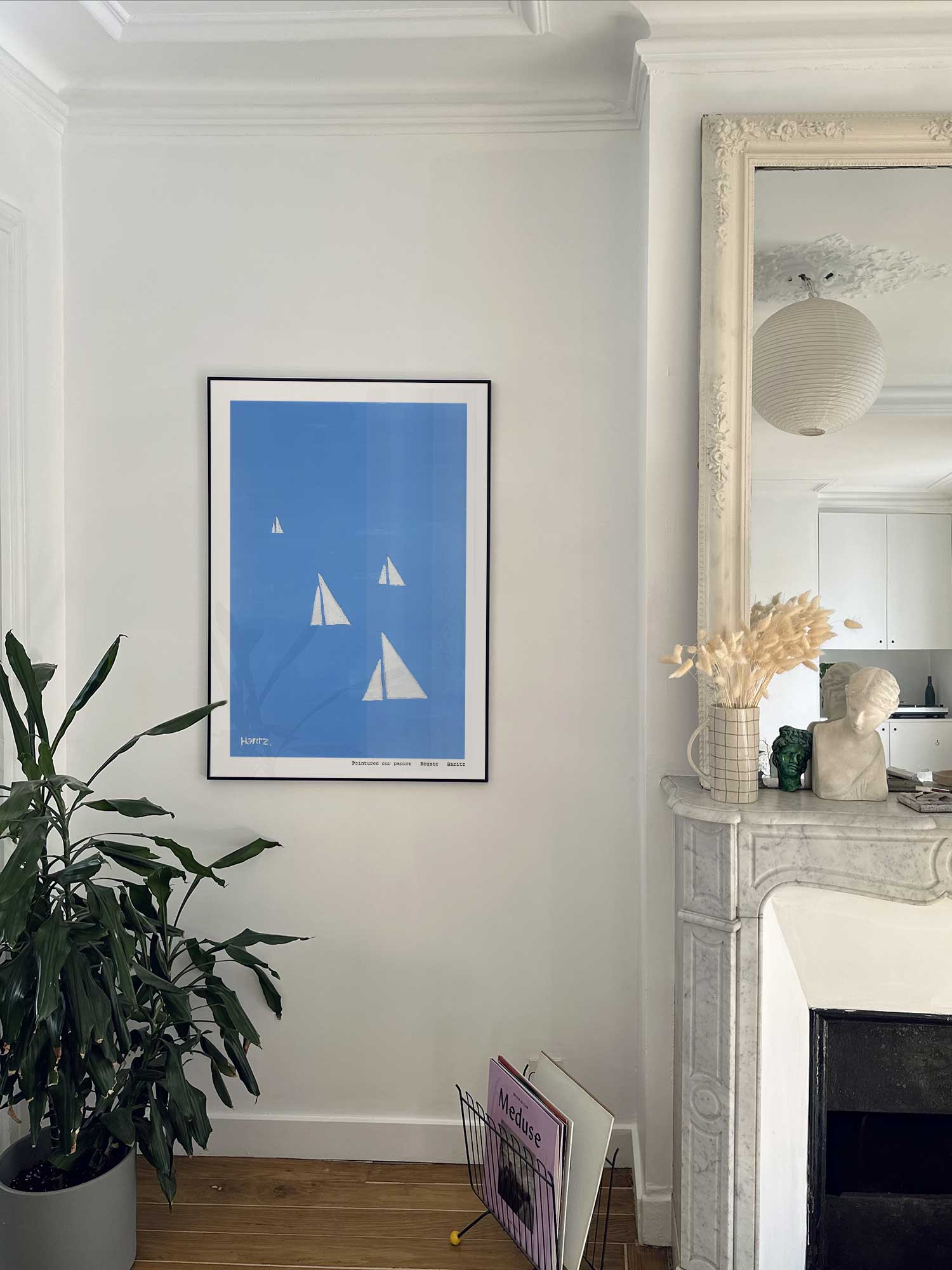 Affiche Régate de Haritz accrochée au mur près d'une cheminée en marbre dans un appartement parisien.