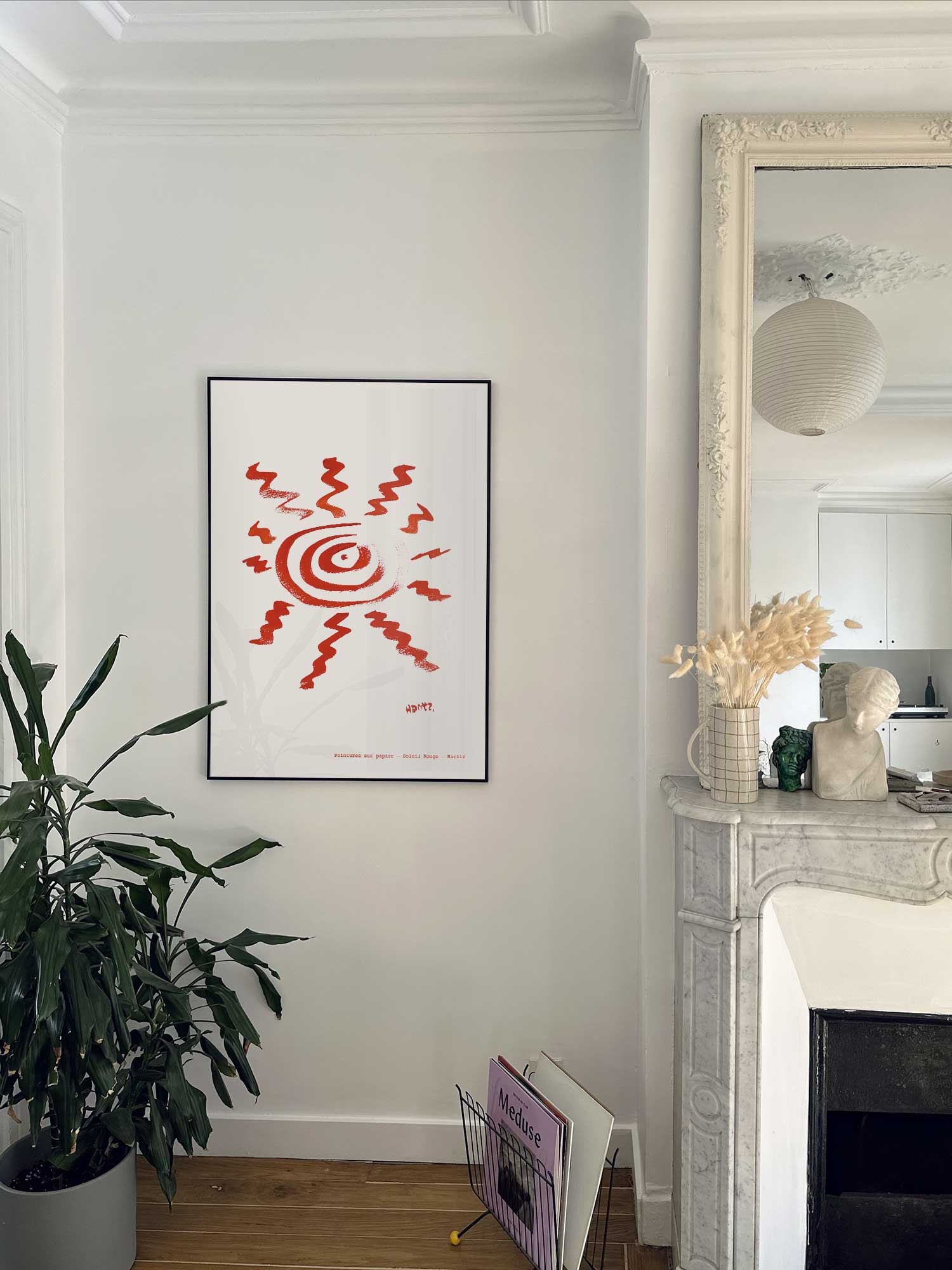 Affiche Soleil rouge de Haritz accrochée au mur près d'une cheminée en marbre dans un appartement parisien.