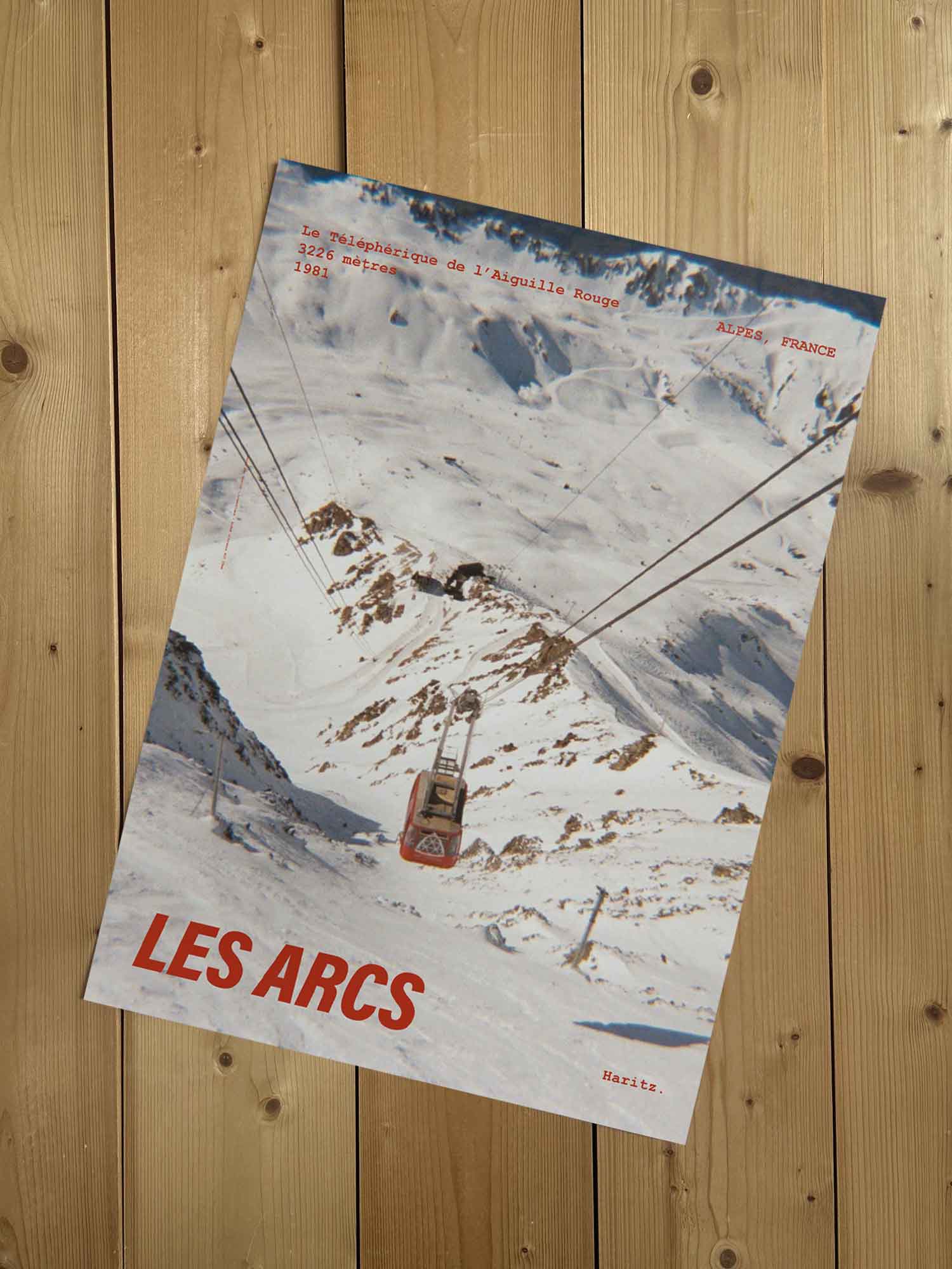 Affiche Les Arcs vintage sans cadre posée sur parquet bois — téléphérique de l'Aiguille Rouge 3226 mètres, photographie argentique Haritz