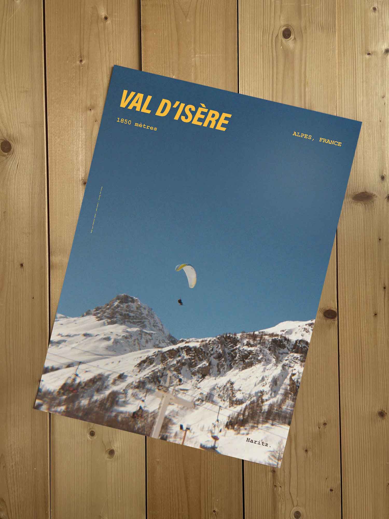 Affiche Val d'Isère vintage sans cadre posée sur parquet bois — parapente jaune au-dessus des pistes de Val d'Isère, photographie argentique Haritz