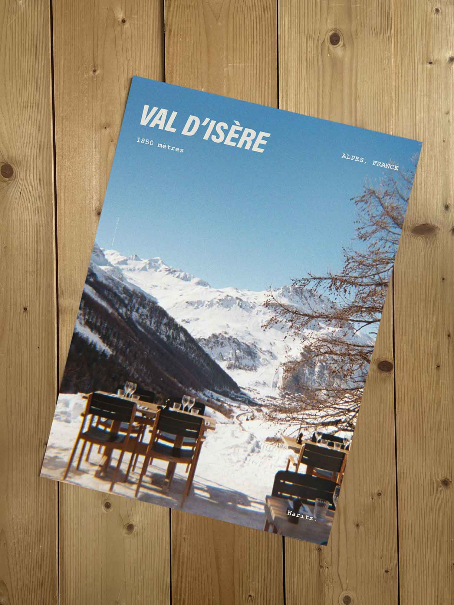 Affiche Val d'Isère vintage sans cadre posée sur parquet bois — terrasse dressée en altitude avec vue sur les massifs, photographie argentique Haritz