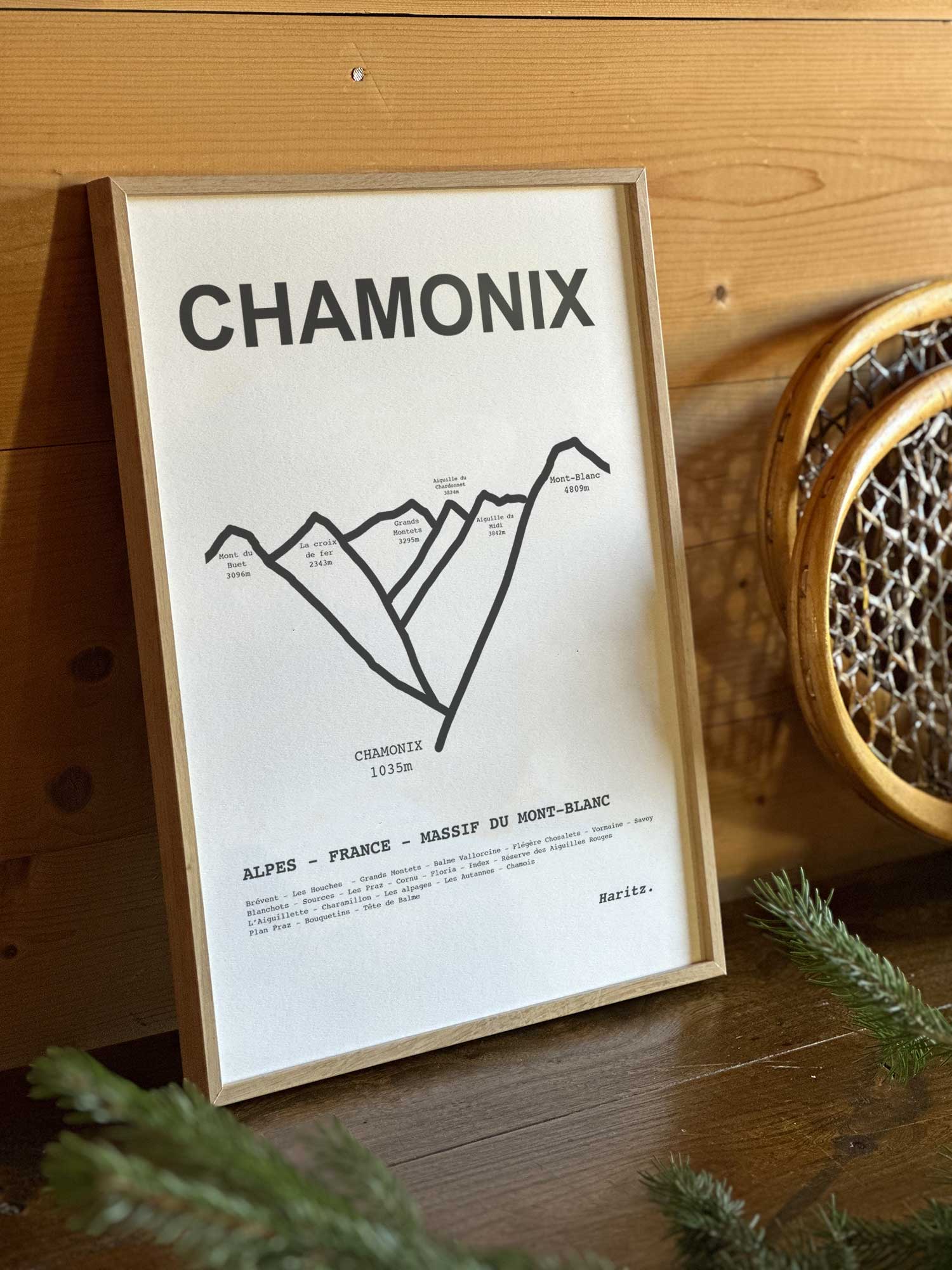 Affiche Chamonix du tracé topographique des sommets dans un cadre en bois naturel, mise en scène dans une décoration chalet avec objets vintage et raquettes à neige, par Haritz.
