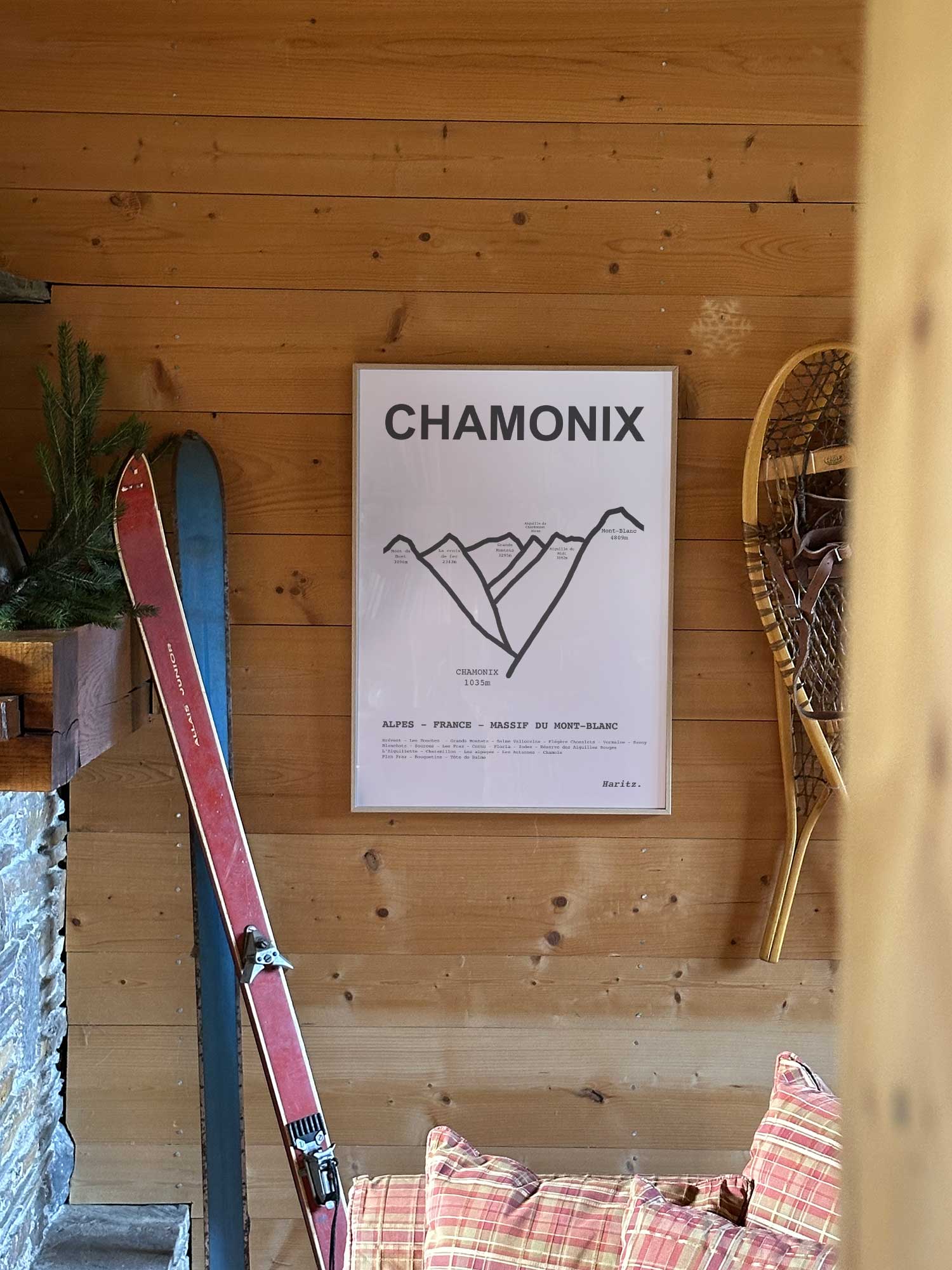 Affiche Chamonix représentant les sommets de la station, accrochée au mur d’un salon de chalet avec skis vintage et raquettes à neige, décoration montagne Haritz.