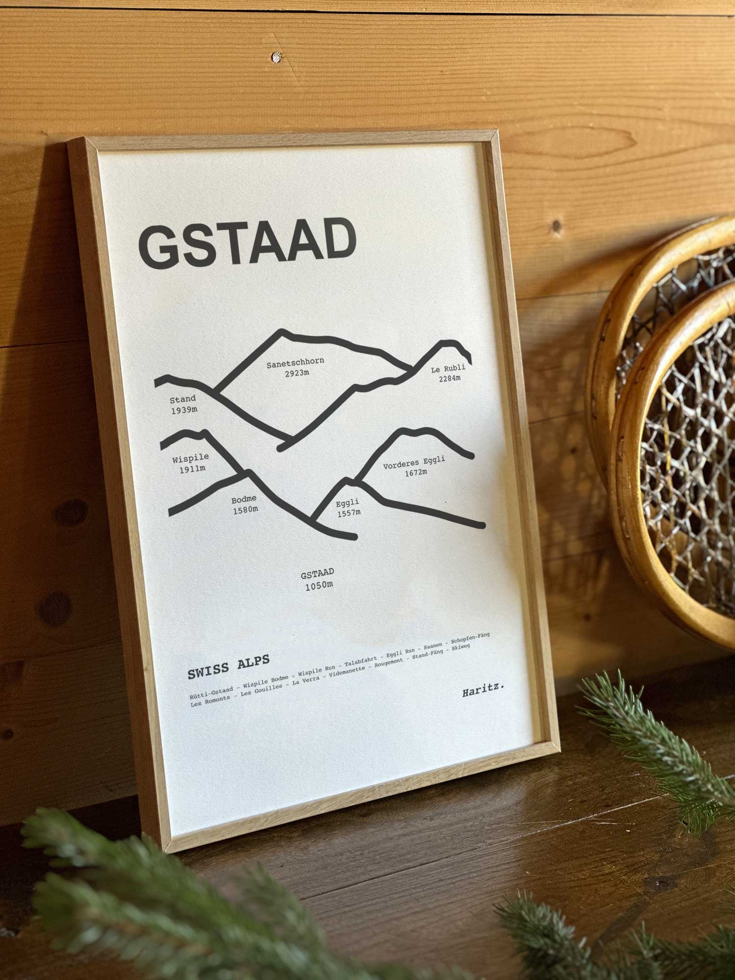 Affiche Gstaad du tracé topographique des sommets dans un cadre en bois naturel, mise en scène dans une décoration chalet avec objets vintage et raquettes à neige, par Haritz.