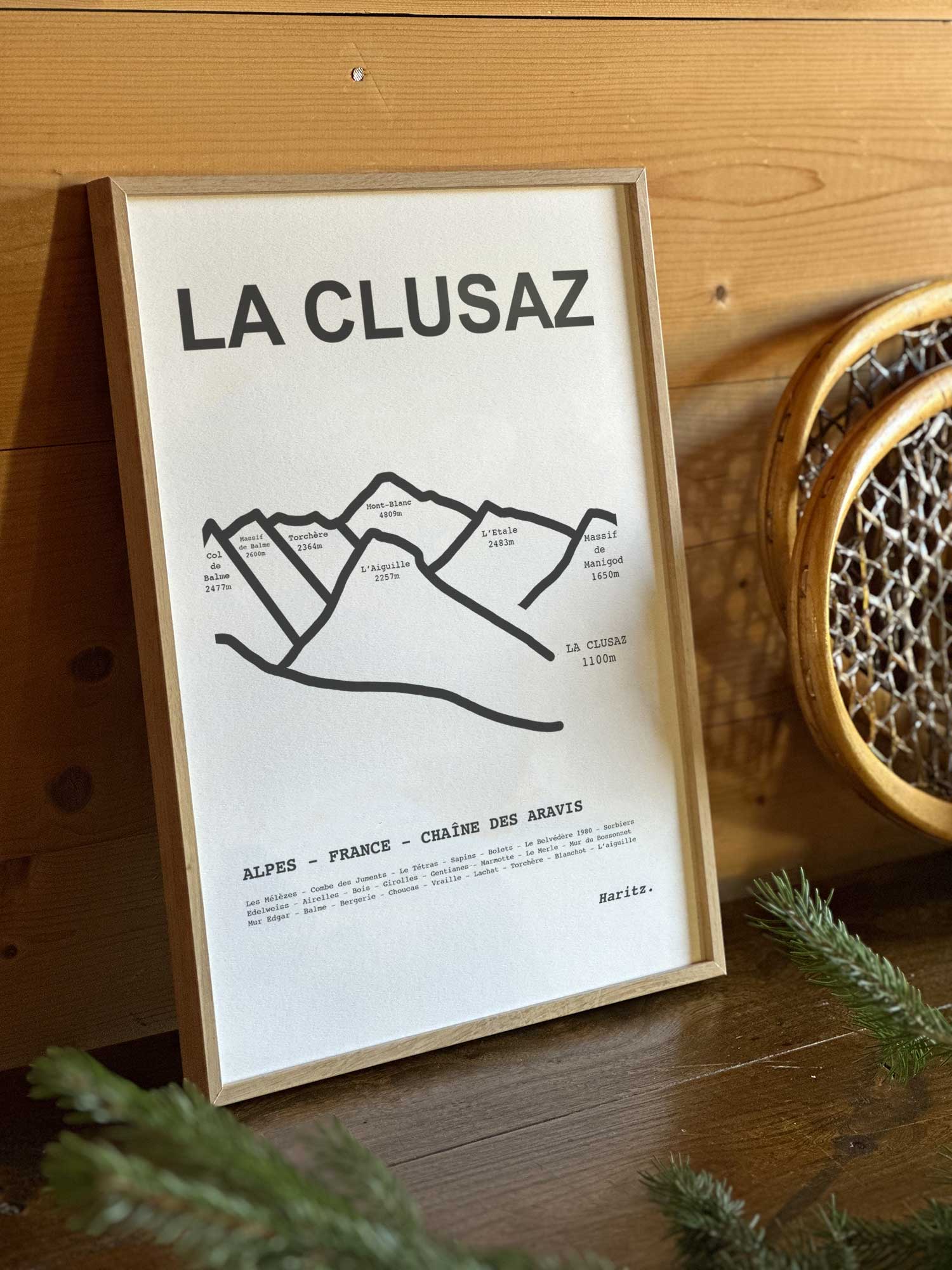 Affiche La Clusaz du tracé topographique des sommets dans un cadre en bois naturel, mise en scène dans une décoration chalet avec objets vintage et raquettes à neige, par Haritz.