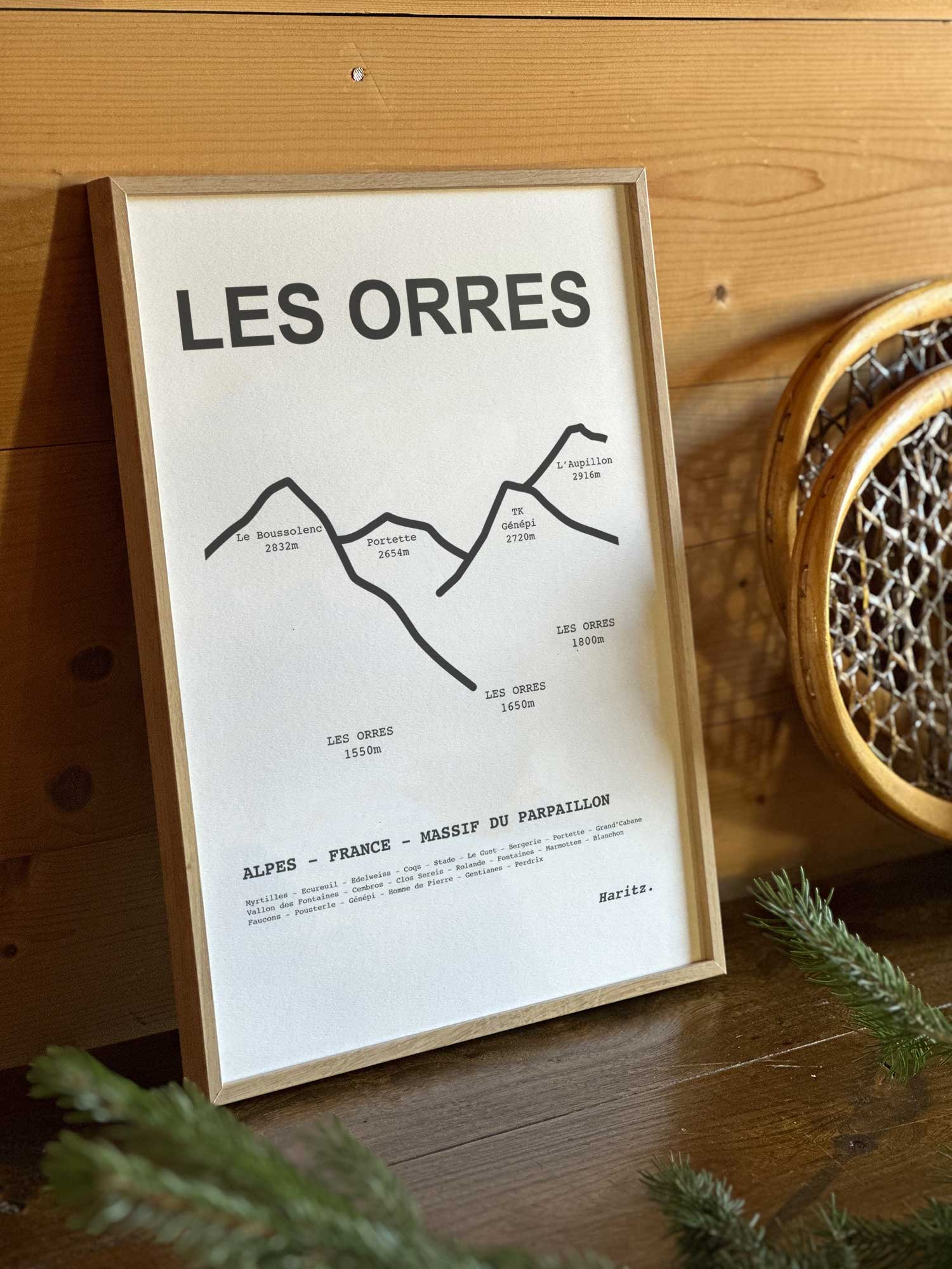 Affiche Les Orres du tracé topographique des sommets dans un cadre en bois naturel, mise en scène dans une décoration chalet avec objets vintage et raquettes à neige, par Haritz.