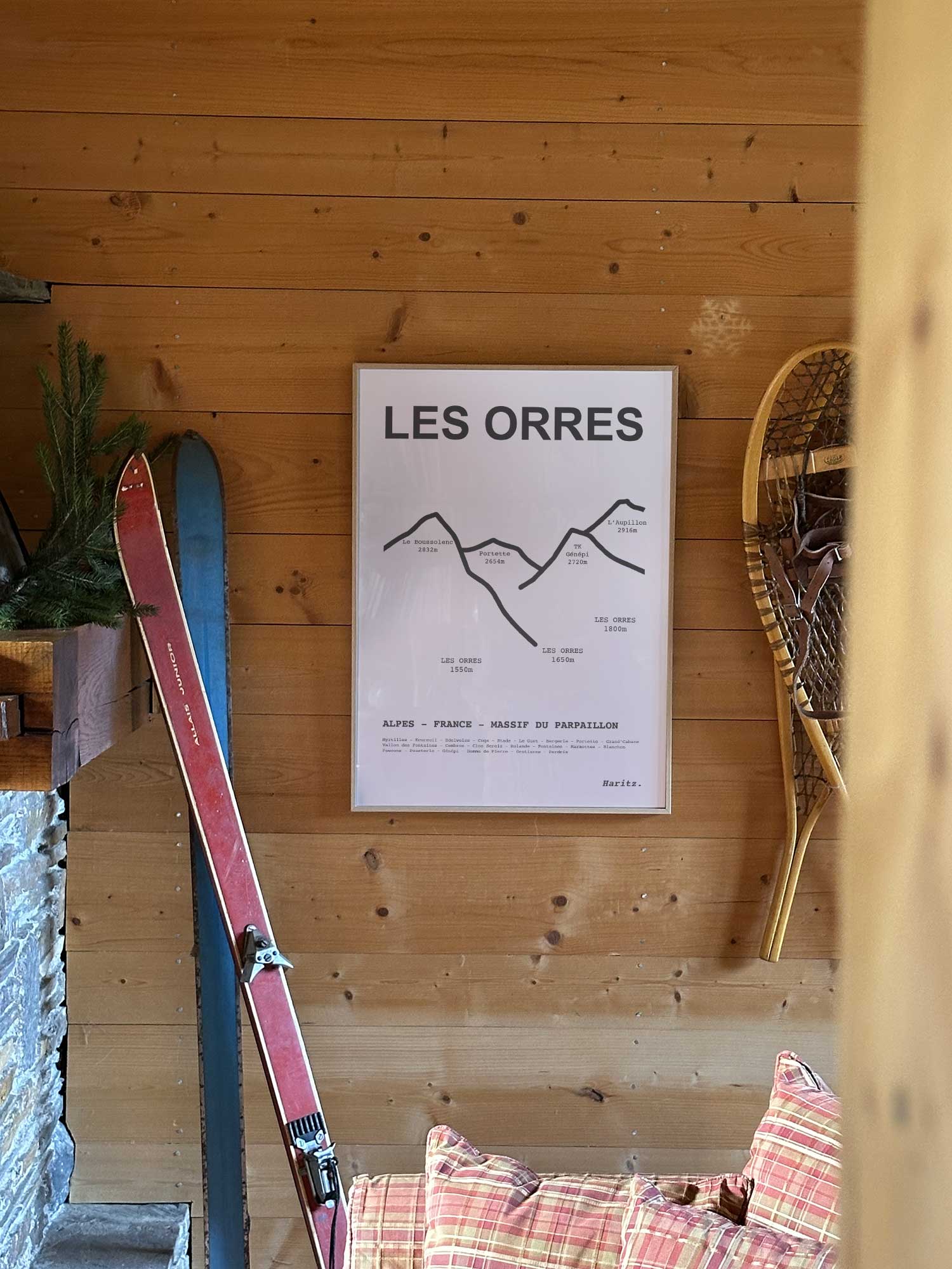 Affiche Les Orres représentant les sommets de la station, accrochée au mur d’un salon de chalet avec skis vintage et raquettes à neige, décoration montagne Haritz.