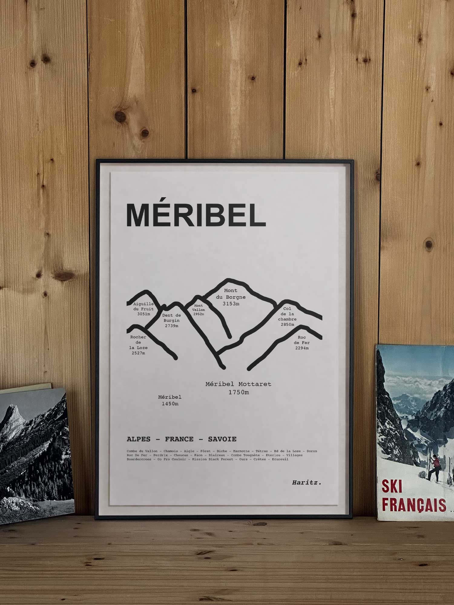 Affiche Méribel représentant le tracé topographique des sommets, encadrée avec un cadre noir et posée sur une étagère en bois dans une décoration chalet montagne, création Haritz.