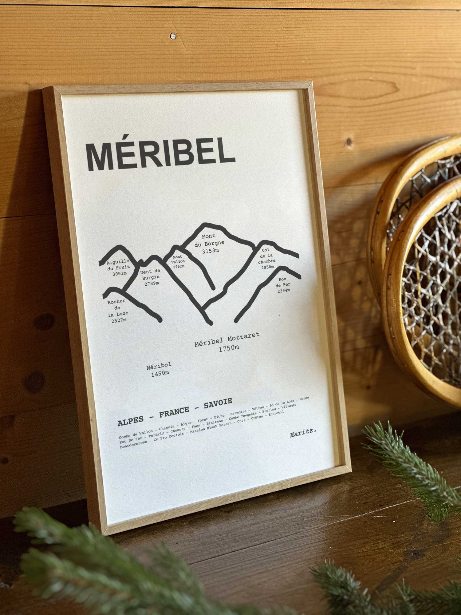 Affiche Méribel du tracé topographique des sommets dans un cadre en bois naturel, mise en scène dans une décoration chalet avec objets vintage et raquettes à neige, par Haritz.