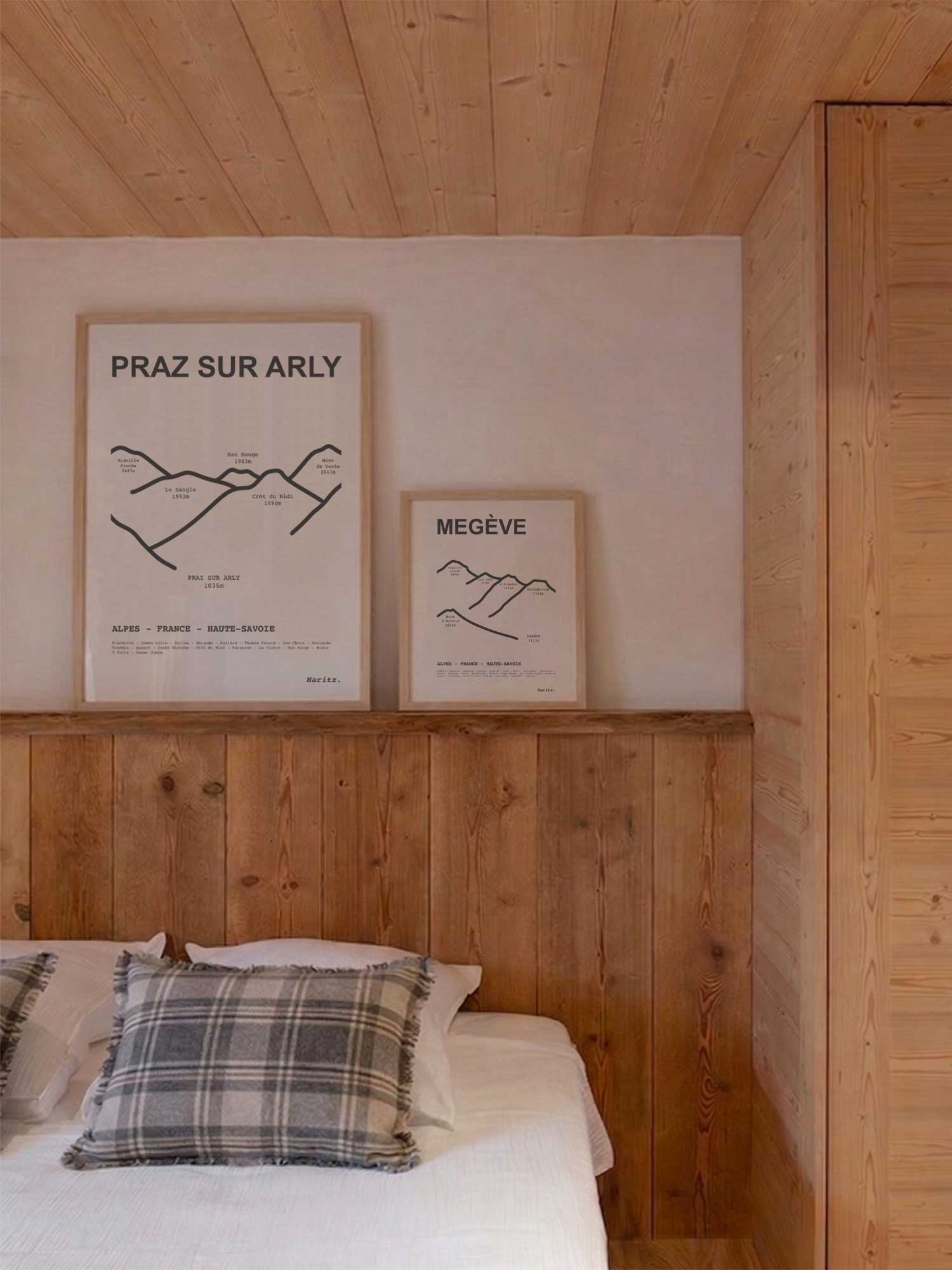 Affiches Praz sur Arly et Megève représentant les sommets des stations, encadrées posées au-dessus d’un lit dans une chambre de chalet de montagne moderne, décoration murale alpine signée Haritz.