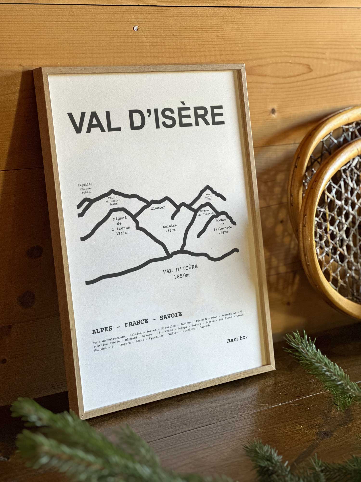 Affiche Val d'Isère du tracé topographique des sommets dans un cadre en bois naturel, mise en scène dans une décoration chalet avec objets vintage et raquettes à neige, par Haritz.