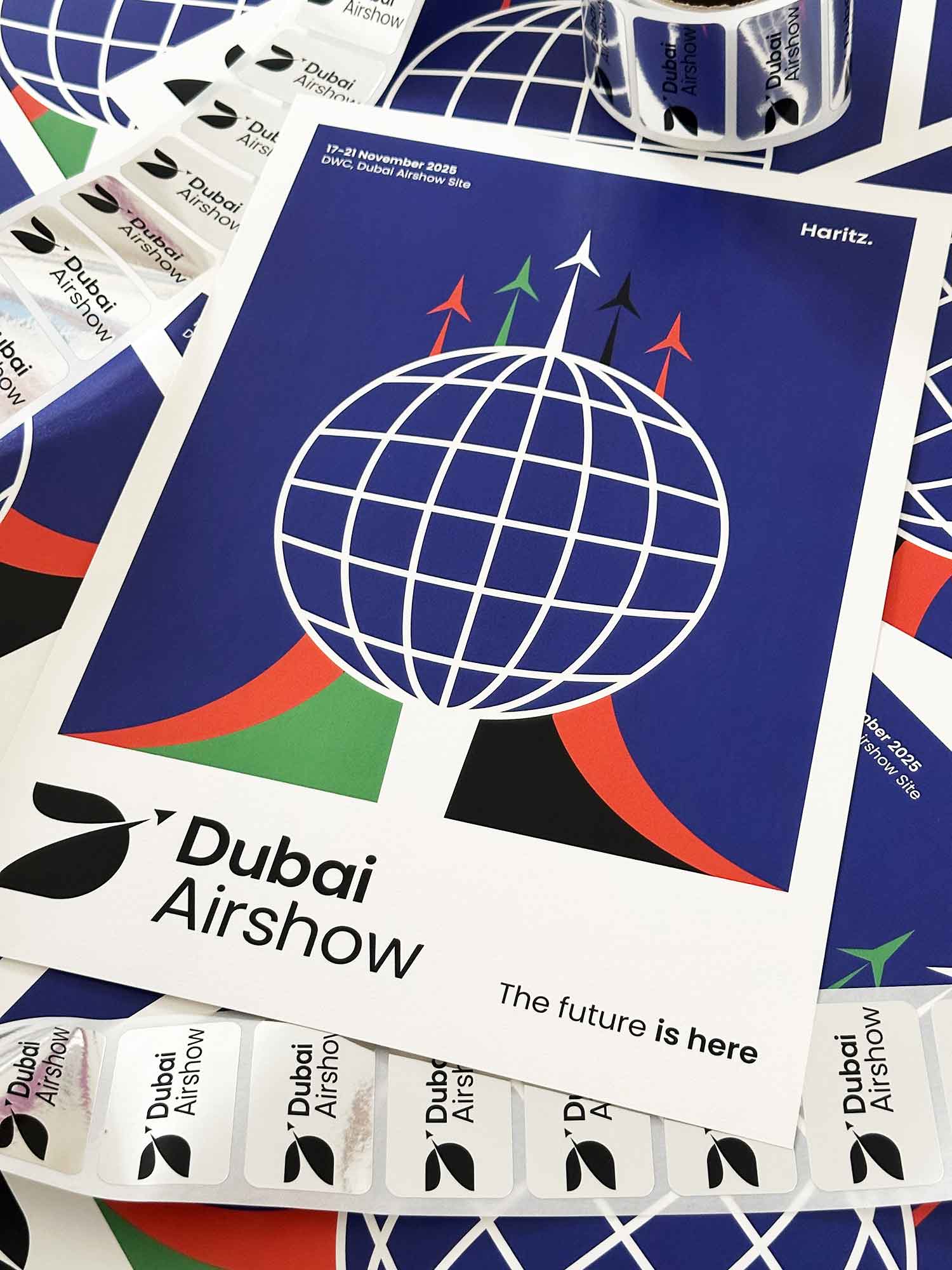 Affiche Dubai Airshow 2025 dessinée par l'artiste Haritz — design graphique avec globe et avions aux couleurs des Émirats, entourée de stickers et merchandising officiel du salon aéronautique